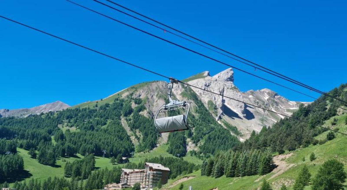 Télésiège au premier plan, paysage montagnard verdoyant avec quelques névés en altitude - Télésiège au premier plan, paysage montagnard verdoyant avec quelques névés en altitude